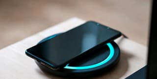 Smartphone sitting on a Qi wireless charging pad with a soft blue light indicator