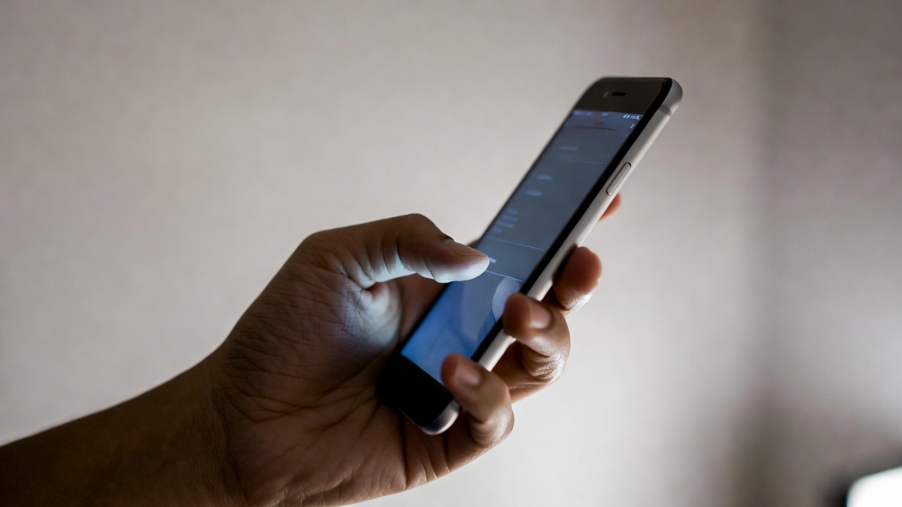 Close-up of a hand holding a smartphone with the screen lit up, relaxed grip suggesting calm and intentional use