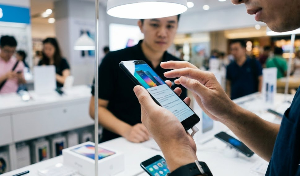 Person inspecting iPhone screen for cracks under light before purchase